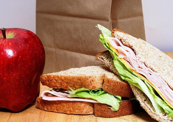 A brown paper bag lunch with a sandwich and apple in front