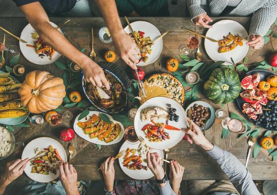 Flat-lay of friends or family feasting at Thanksgiving Day festive table with turkey, pumpkin pie, roasted seasonal vegetables and fruit, top view