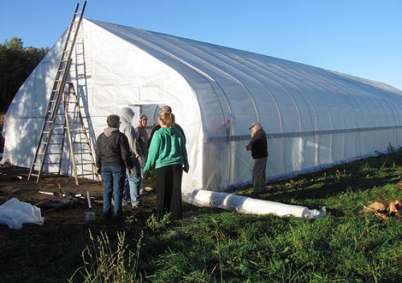 A group finishes putting the outer skin on a hoop house in Michigan. The hoop house has helped local farmers lengthen the short Michigan growing season by two full months, giving them additional crops to sell at winter markets.  Photo courtesy Brittain Family Farms.