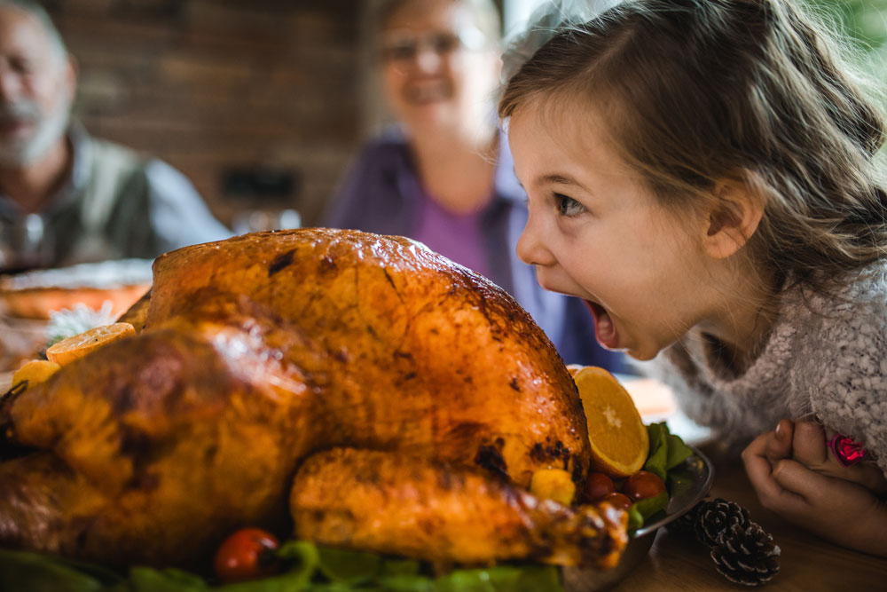 A girl with her mouth wide open near the turkey on a table