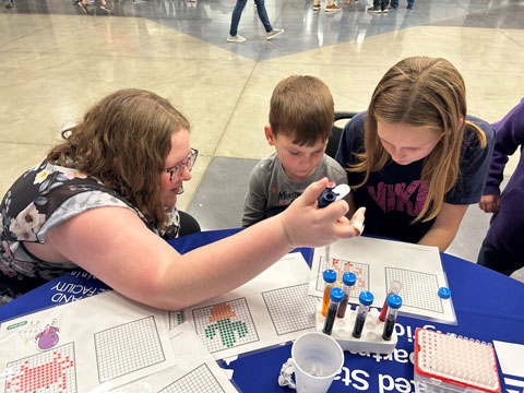 Kaite Merino, biological science laboratory technician, shows kids at Rock Creek STEAM Night how to pipet liquid — a common science practice — as part of an art activity