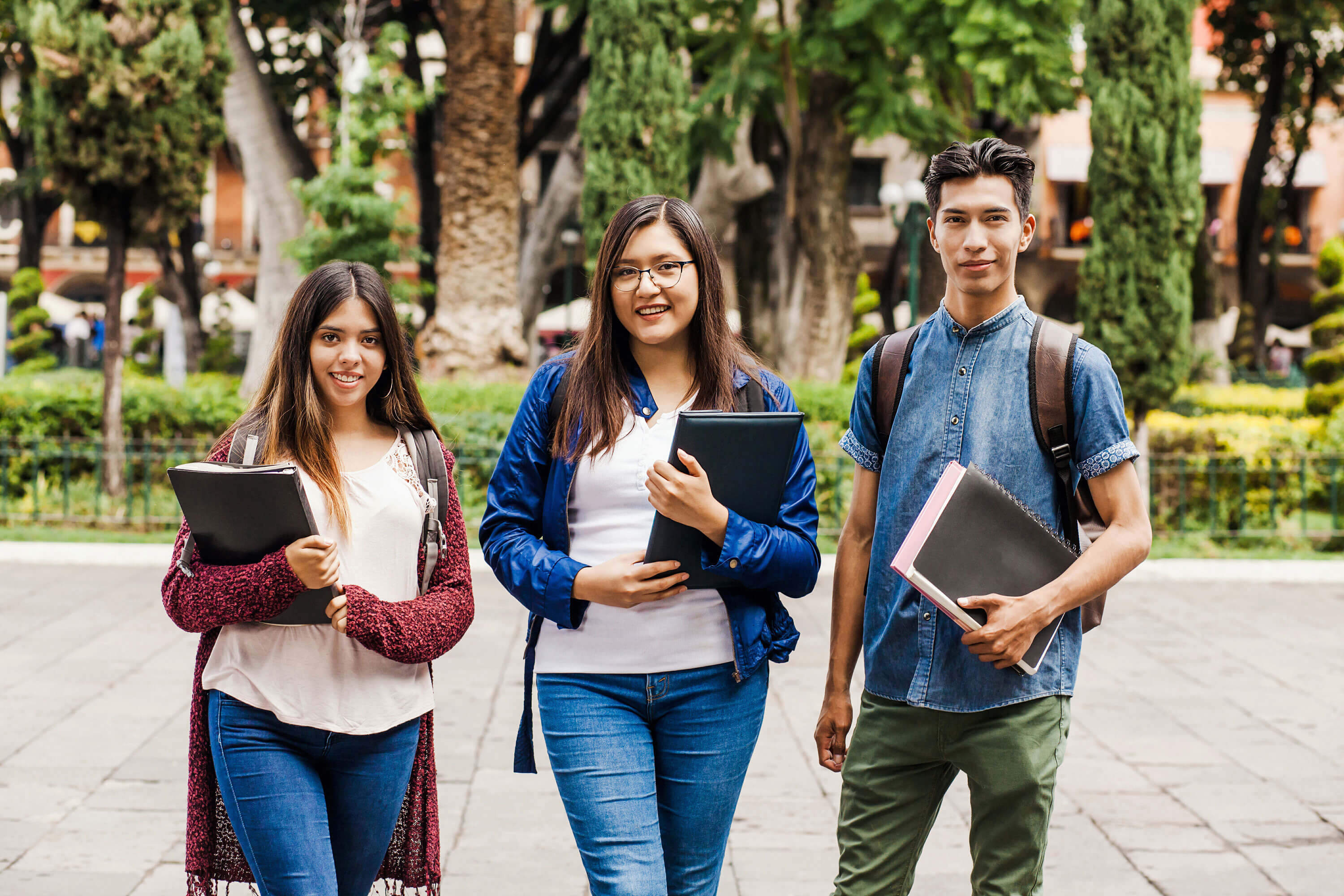 A group of three Hispanic students holding books