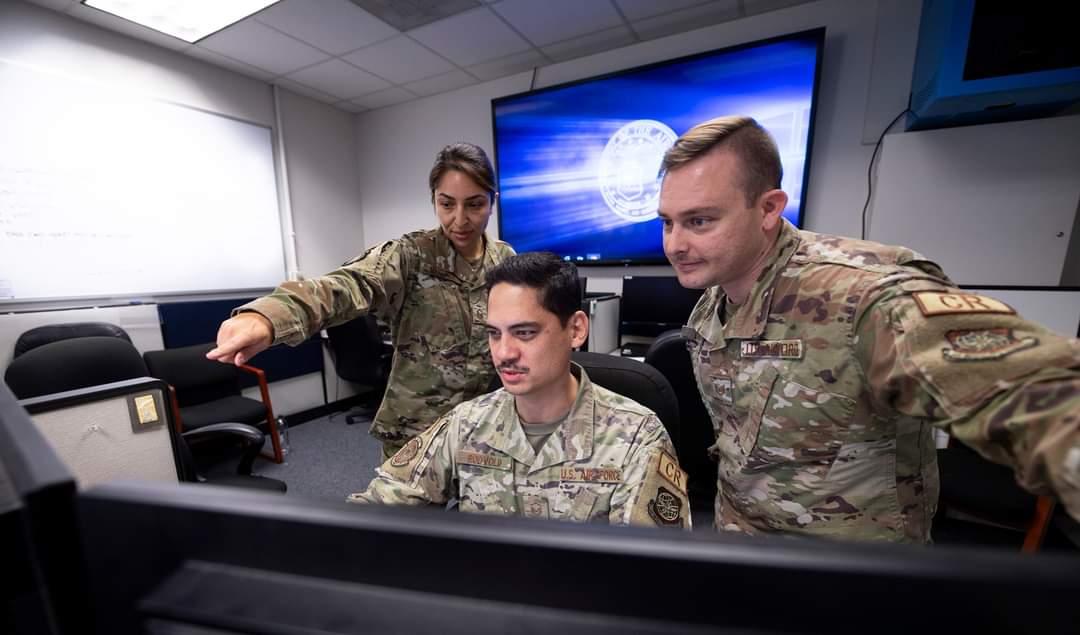 A photo of Master Sergeant BreAnna Martinez working with two other military members behind a computer