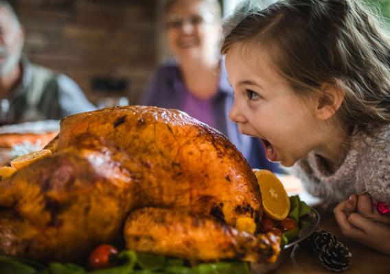 A girl with her mouth wide open near the turkey on a table