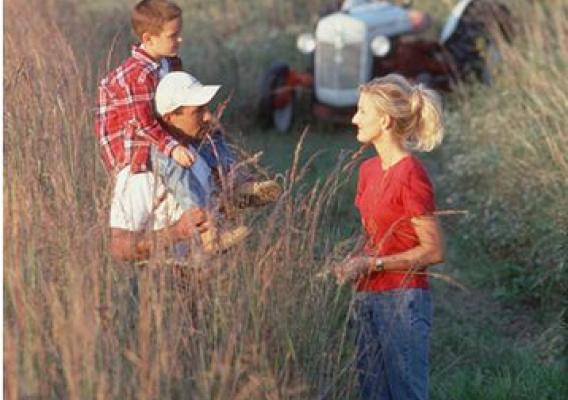 A family stands in a plot of tall grass plantings on a farm in central Iowa. NRCS photo.
