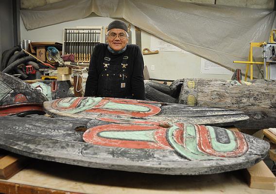 Tlingit Master Carver Wayne Price of Haines stands near the totem he is restoring. The totem has overlooked the Auke Recreation Area for more than 70 years. (U.S. Forest Service photo by Laurie Craig)