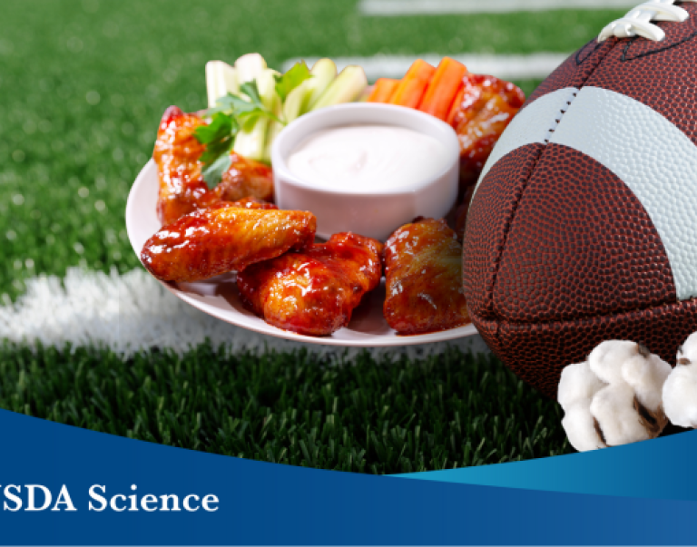 A photo on a sports field with a plate of chicken wings and vegetables, a football, and cotton in the forefront. A blue banner with the text “USDA Science” is overlaying the picture